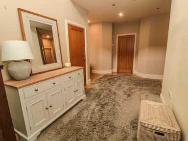 A hallway with a white sideboard mirror lamp wicker basket and two wooden doors at Fontburn Farmhouse in Ewesley near Rothbury