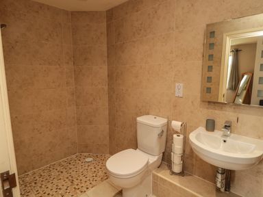 A bathroom with a toilet a sink a mirror and a tiled shower area at Fontburn Farmhouse in Ewesley near Rothbury