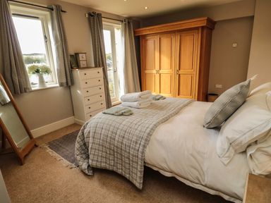 A bedroom with a bed towels and pillows a wooden wardrobe and a chest of drawers at Fontburn Farmhouse in Ewesley near Rothbury