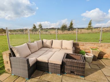 An outdoor patio area with a wicker corner sofa with beige cushions and potted plants at Fontburn Farmhouse in Ewesley near Rothbury