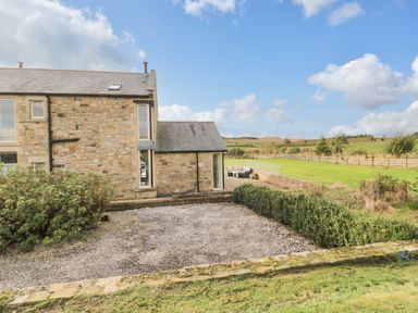 A stone farmhouse with a gravel driveway and green hedge next to a grassy field at Fontburn Farmhouse Ewesley near Rothbury