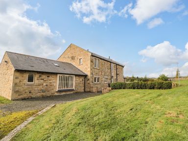 A stone farmhouse with multiple windows and a gravel path surrounded by grass at Fontburn Farmhouse in Ewesley near Rothbury
