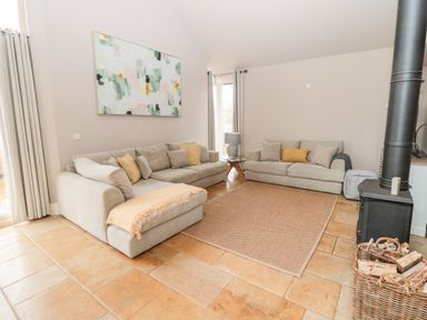 A living room with two beige sofas a wood burning stove and a basket of firewood at Fontburn Farmhouse in Ewesley near Rothbury
