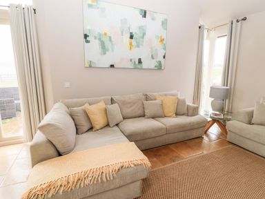 A living room with a beige corner sofa cushions a side table with a lamp and abstract painting on the wall at Fontburn Farmhouse Ewesley near Rothbury