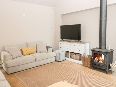 A living room with a sofa a television on a cabinet a rug and a wood burning stove at Fontburn Farmhouse in Ewesley near Rothbury