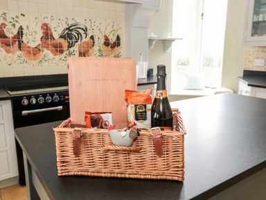 A kitchen counter with a wicker basket containing snacks and a bottle with a tiled backsplash showing roosters at Fontburn Farmhouse in Ewesley near Rothbury