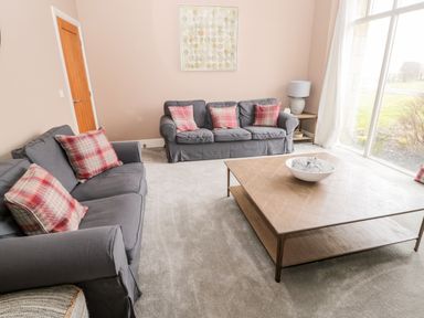 A sitting room with two gray sofas red plaid cushions a wooden coffee table with a white bowl and a window with curtains at Fontburn Farmhouse in Ewesley near Rothbury