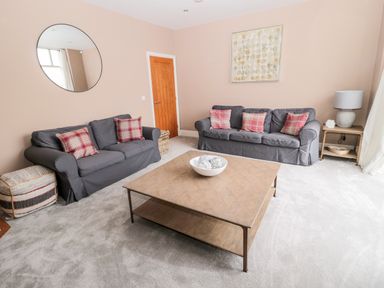 A living room with two sofas with plaid cushions a wooden coffee table a round wall mirror and a side table with a lamp at Fontburn Farmhouse in Ewesley near Rothbury