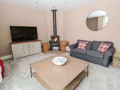A living room with a gray sofa with plaid cushions a wooden coffee table a wood burning stove and a television on a cabinet at Fontburn Farmhouse in Ewesley near Rothbury