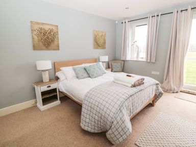 A bedroom with a double bed bedside tables lamps and a chair near window at Fontburn Farmhouse in Ewesley near Rothbury