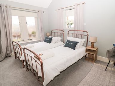 A bedroom with two single beds with metal frames a wooden nightstand with a lamp a window with curtains and a vase with flowers at Fontburn Farmhouse in Ewesley near Rothbury