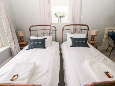 A bedroom with two single beds with white bedding and dark pillows beside a window with flowers at Fontburn Farmhouse in Ewesley near Rothbury