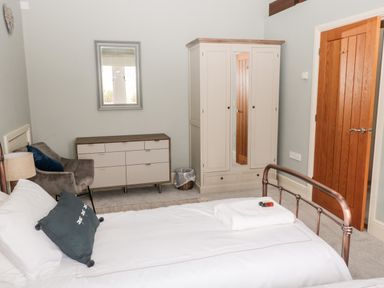 A bedroom with a bed towel and mini toiletries a wardrobe a white dresser a chair a wooden door and a wall mirror at Fontburn Farmhouse in Ewesley near Rothbury