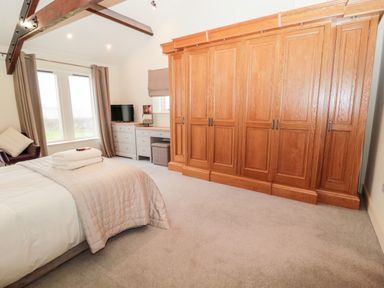 A bedroom with a bed folded towels a large wooden wardrobe a desk chair and windows with curtains at Fontburn Farmhouse in Ewesley near Rothbury