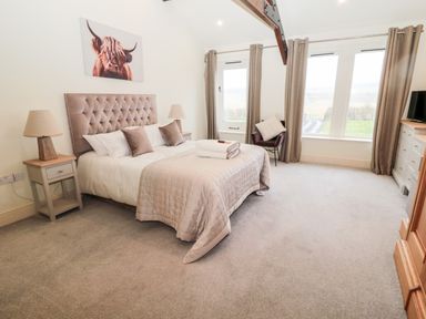 A bedroom with a bed bedside tables lamps a chair and windows with curtains at Fontburn Farmhouse in Ewesley near Rothbury