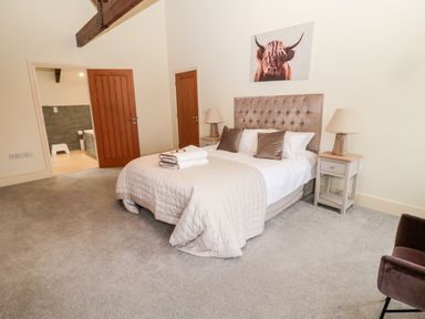 A bedroom with a double bed two bedside tables with lamps an armchair and an open door to a bathroom at Fontburn Farmhouse in Ewesley near Rothbury