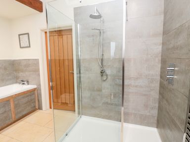 A bathroom with a glass shower enclosure a bathtub and a wooden door at Fontburn Farmhouse in Ewesley near Rothbury