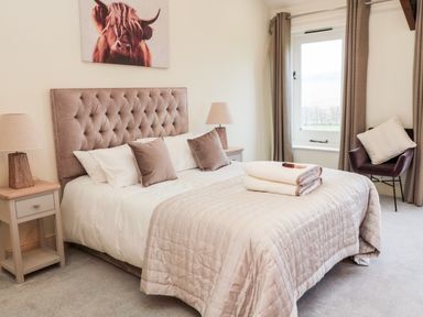 A bedroom with a bed two bedside tables with lamps a window and a chair at Fontburn Farmhouse Ewesley near Rothbury
