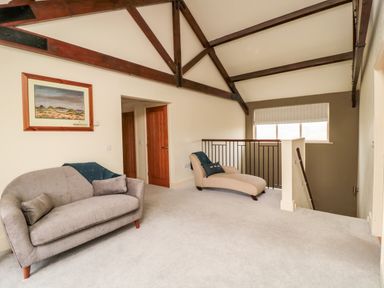 A sitting area with a sofa and chaise lounge under a vaulted ceiling with exposed wooden beams at Fontburn Farmhouse in Ewesley near Rothbury
