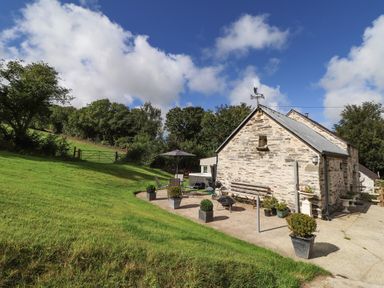 A stone house with a patio area and garden furniture on a grassy hillside at Y Felin at Coed Cadw in Felindre Farchog near Newport Pembrokeshire