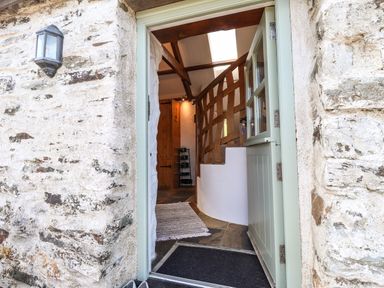 An open door showing a stone wall exterior and an interior with wooden beams and a white curved staircase at Y Felin at Coed Cadw in Felindre Farchog near Newport Pembrokeshire