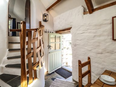 A stairway with a wooden railing next to a half-open door and a wooden chair near a table at Y Felin at Coed Cadw in Felindre Farchog near Newport Pembrokeshire