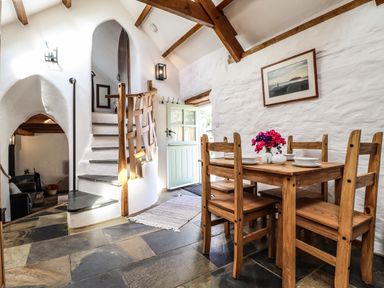 A dining area with wooden table and chairs next to a staircase and open door at Y Felin at Coed Cadw Felindre Farchog near Newport Pembrokeshire