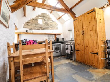 A kitchen with wooden table and chairs stone floor wooden ceiling beams and appliances at Y Felin at Coed Cadw in Felindre Farchog near Newport Pembrokeshire