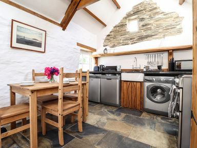 A kitchen with wooden dining table and chairs and appliances including a washing machine at Y Felin at Coed Cadw in Felindre Farchog near Newport Pembrokeshire