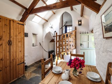 A dining area with a wooden table set with dishes and flowers and a staircase with wooden railing in a rustic room at Y Felin at Coed Cadw in Felindre Farchog near Newport Pembrokeshire
