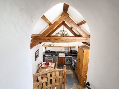 A kitchen with wooden beams a dining table with chairs and appliances at Y Felin at Coed Cadw in Felindre Farchog near Newport Pembrokeshire