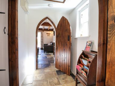 A hallway with a wooden arched door leading to a living room with sofas and a window at Y Felin at Coed Cadw in Felindre Farchog near Newport Pembrokeshire