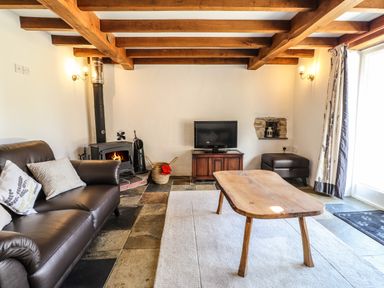 A living room with wooden beams on the ceiling a leather sofa a wood stove a wooden coffee table and a television stand at Y Felin at Coed Cadw in Felindre Farchog near Newport Pembrokeshire