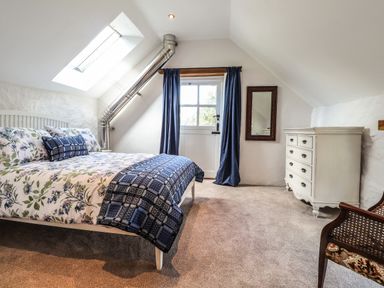 A bedroom with a bed with floral bedding a white dresser a window with blue curtains and a chair at Y Felin at Coed Cadw Felindre Farchog near Newport Pembrokeshire
