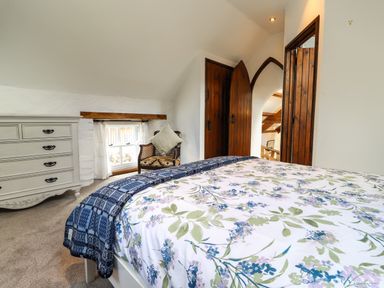 A bedroom with a floral bedspread a blue throw a white chest of drawers a wooden chair with a cushion and wooden doors at Y Felin at Coed Cadw in Felindre Farchog near Newport Pembrokeshire