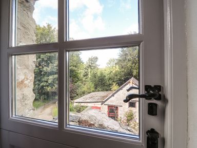 View through a window showing an old stone building with red doors and surrounding trees at Y Felin at Coed Cadw in Felindre Farchog near Newport Pembrokeshire