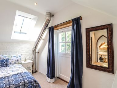 A bedroom with a bed beside a small white nightstand and a mirror reflecting a room with wooden beams at Y Felin at Coed Cadw in Felindre Farchog near Newport Pembrokeshire