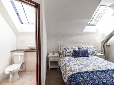A bedroom with a floral bedspread and bedside tables next to a bathroom with a toilet and sink at Y Felin at Coed Cadw in Felindre Farchog near Newport Pembrokeshire