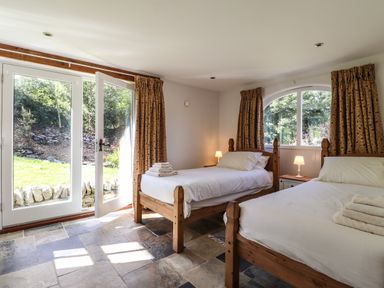 A bedroom with two single wooden beds next to large glass doors and a window at Y Felin at Coed Cadw in Felindre Farchog near Newport Pembrokeshire