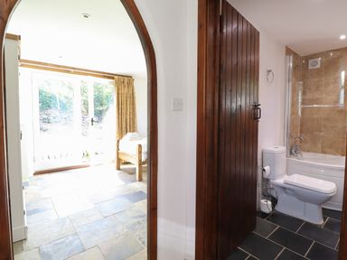 A bathroom with toilet and bathtub next to a bedroom with bed and glass door at Y Felin at Coed Cadw in Felindre Farchog near Newport Pembrokeshire
