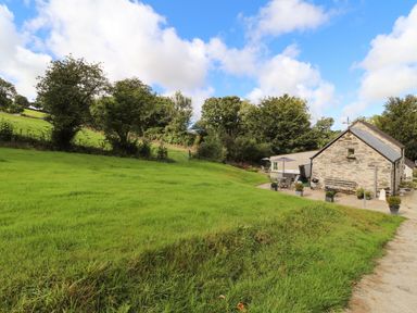 A grassy yard with trees and a stone building with an outdoor seating area at Y Felin at Coed Cadw in Felindre Farchog near Newport Pembrokeshire