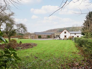 A green lawn with a white house and wooden barn in the background at Maes Y Berllan Barn in Gilwern