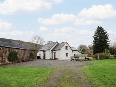 A white stone house with a slate roof next to a wooden barn and a gravel driveway at Maes Y Berllan Barn in Gilwern