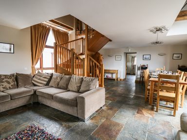 A living room with a sectional sofa and staircase next to a dining area with a wooden table and chairs at Maes Y Berllan Barn in Gilwern