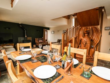 A dining table set with plates and glasses in a living room with a wooden staircase and a carved wooden dragon at Maes Y Berllan Barn in Gilwern