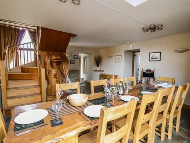 A dining room with a wooden table and chairs near a staircase with a wooden dragon carving at Maes Y Berllan Barn Gilwern