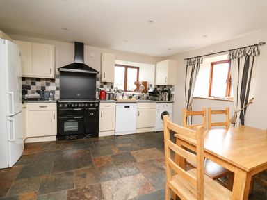 A kitchen with wooden dining table chairs white cabinets and appliances at Maes Y Berllan Barn in Gilwern