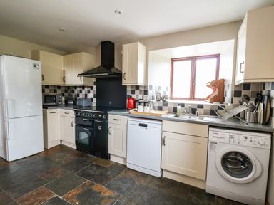 A kitchen with white cabinets a black stove a refrigerator dishwasher and washing machine at Maes Y Berllan Barn in Gilwern