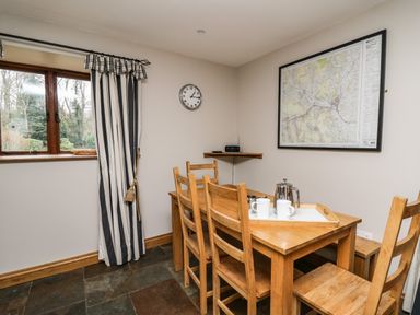 A dining area with wooden table and chairs cups kettle on table map on wall and window with striped curtains at Maes Y Berllan Barn in Gilwern