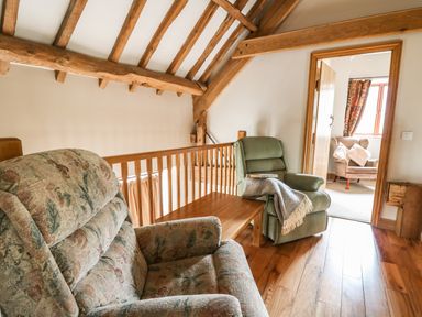 A seating area with two armchairs a wooden table and wooden beams on the ceiling at Maes Y Berllan Barn in Gilwern